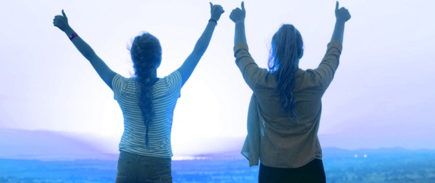 Two women standing with arms and thumbs up